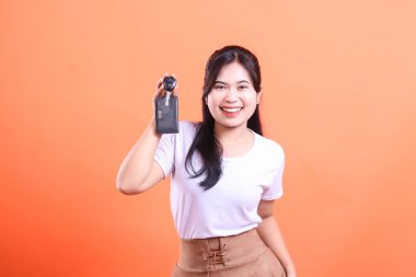 Gülümseyen ve yeni araba anahtarlarını tutan genç bir Asyalı kadın çok mutlu ve heyecanlı. turuncu arkaplanda izole.