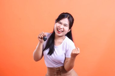 Çekici, gülümseyen bir kadın arabanın anahtarını neşeli bir ifadeyle tutuyor. Çok heyecanlı ve mutlu görünüyor, turuncu arka planda soyutlanmış.