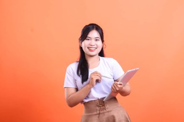 Mutlu Asyalı kadın dijital tablet kullanıyor ve kameraya gülümsüyor. Modern kadın çalışıyor. turuncu arkaplanda izole.