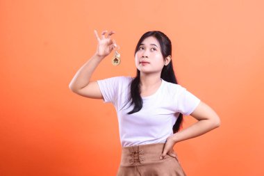 Genç bir kadın rüya gibi gözlerle, evin anahtarlarını tutarken düşünceli bir ifadeyle, turuncu arka planda izole bir şekilde yukarı bakar..