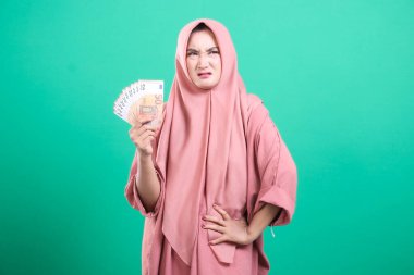 Mutsuz bir Arap kadın ve bir yığın avro banknotları mali ve para konularındaki hayal kırıklığını gösteriyor. Yeşil arka planda izole edilmiş, maddi zorluklar hakkında endişelerini dile getiriyor.