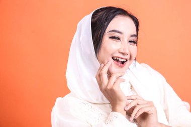 Güzel ve neşeli, tesettürlü genç bir müslüman kadının portresi. Görünüşüne özgüven ve neşe katıyor. turuncu bir arkaplanda izole.