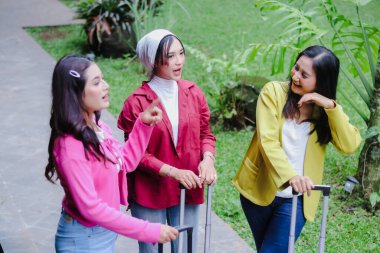 Üç genç bayandan oluşan bir grup dışarıda bagajlarıyla sohbet ederken görülüyor. Maceralarını planlarken neşe saçıyorlar. Renkli kıyafetler neşeli atmosferi güçlendirir..