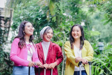 Üç kadın maceralarına başlamadan önce neşe dolu bir anı paylaşıyorlar. Canlı renkler içinde, doğanın ortasında duruyorlar, bagajları hazır, pozitif enerji ve coşku yayıyorlar..