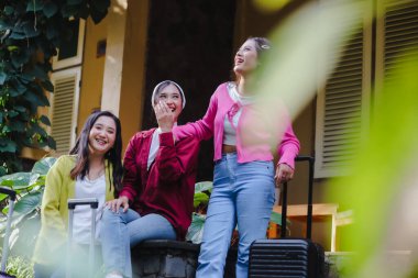 Sevinç saçan üç genç kadın bir an kahkaha atarlar, arkadaşlığın ve seyahat heyecanının özünü somutlaştırırlar. Bavulları hazır, eğlenceli bir tatil bekliyorlar..