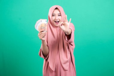 Finansal başarıyı kutlayan neşeli Müslüman kadın avro banknotları hayranı ve yeşil arka planda izole edilmiş 
