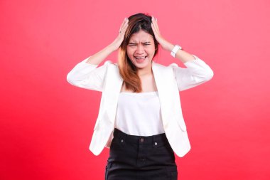 Çerçevede beyaz ceket, beyaz bluz ve siyah etek giyen, elleri başının üstünde olan bir kadın görülüyor, kırmızı arka planda izole edilmiş.