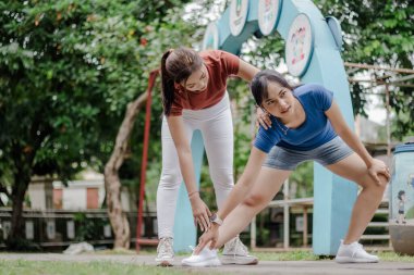İki genç bayan dışarıda esniyorlar. Biri diğerine yardım ediyor. Gülümsüyorlar ve mutlu görünüyorlar, antrenmanlarına hazırlanıyorlar. Sabahleyin parkta..