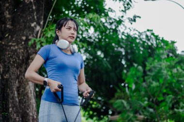 Bir kadın direnç bantlarını doğal ortamında güç antrenmanı için kullanır. Bir sonraki mücadelesine kararlı bir şekilde odaklanır. Sabahleyin parkta..