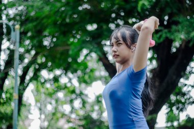 Eğitimdeyken, güç ve dayanıklılık kavramını kullanırken ve dışarıda egzersiz yaparken odaklanmış bir kadın halterle egzersiz yapıyor. Sabahleyin parkta.