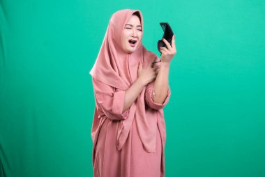 Elinde aynası olan, şaşırmış ve şok olmuş Müslüman bir kadının portresi, yeşil bir arka planda izole edilmiş, dehşeti ifade ediyor..