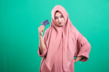 Geleneksel giysiler içinde kredi kartı tutan mutsuz müslüman kadın, yeşil arka planda izole edilmiş borç yüzünden üzgün ve hayal kırıklığına uğramış görünüyor..