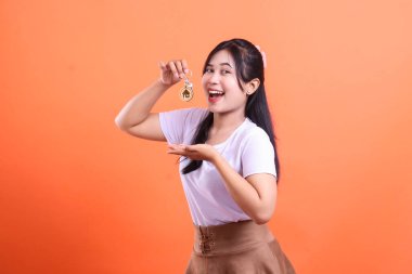 Koyu renk saçlı genç bir kadın neşe içinde evinin anahtarlarını tutuyor. Yeni evine taşınmaya hazır yeni bir evi ve başarıyı simgeliyor. turuncu arkaplanda izole