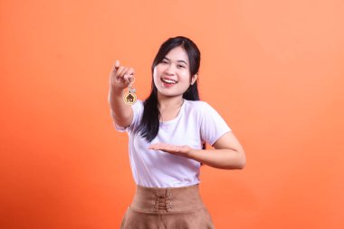 Gülümseyen bir kadın elinde ev sahipliğini temsil eden bir anahtar tutuyor ve elini uzatarak diğerlerini taşınmaya davet ediyor. turuncu arkaplanda izole