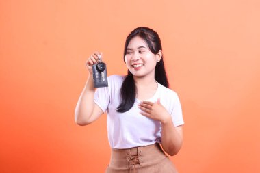 Yeni bir araba aldıktan sonra neşeli bir ifadeyle arabanın anahtarlarını tutan mutlu genç bir kadın. turuncu arkaplanda izole.