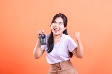 Genç Asyalı kadın çok mutlu, seviniyor ve yeni araba anahtarını tutarak başarıyı kutluyor. turuncu arkaplanda izole.