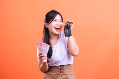 Elinde para ve anahtar tutarken gülümseyen neşeli kadın. Finansal başarı ve yeni araba alımıyla mutlu. turuncu arkaplanda izole