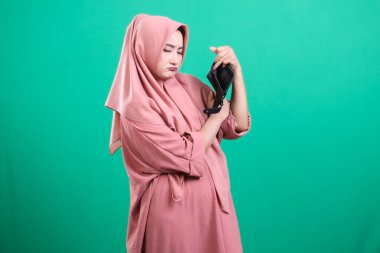 Üzgün kadın cüzdanını gösteriyor, para sıkıntılarını, borçlarını ve finansal sıkıntılarını gösteriyor, yeşil bir arka planda izole edilmiş..