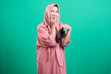 Başörtüsü takan sıkıntılı kadın, yeşil bir arka planda izole edilmiş, mali kriz ve ekonomik belirsizlik temalarını taşıyan boş bir cüzdanı ortaya çıkardı..