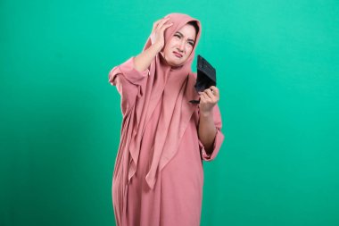 Elinde boş bir cüzdanla tesettürlü genç bir kadın, yeşil arka planda izole edilmiş mali zorlukları ve ekonomik sorunları sembolize ediyor. Belgede tasarruf, harcamalar ve potansiyel iflasla ilgili kaygılar vurgulanıyor.