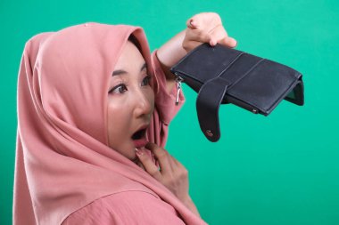 Boş cüzdanına bakan endişeli müslüman kadın. Finansal sorunlar ve para sorunları hakkında şok olmuş ve hayal kırıklığına uğramış. Yeşil bir arkaplanda izole edilmiş.