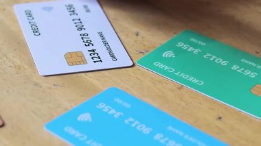 Ahşap bir yüzeyde üç kredi kartının (beyaz, yeşil, mavi) kapatılması, mali işlemlerin, çevrimiçi alışverişin ve temassız ödemelerin sembolize edilmesi.