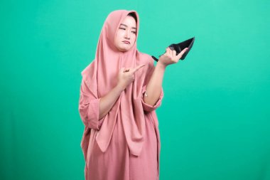 Boş bir cüzdan gösteren tesettürlü sinirli bir kadın: yeşil bir arka planda izole edilmiş, maddi sıkıntı ve kaynak eksikliğini temsil eden.