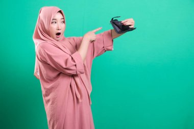 Şok olmuş Müslüman bir kadın, parasal durumundan dolayı hayal kırıklığına uğramış boş bir cüzdan sergiliyor ve yeşil bir arka planda yalnız ve endişeli görünüyor. Ekonomik krizin etkisi.