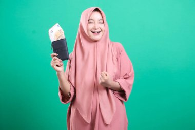 Cüzdanı avro dolu olan heyecanlı bir Müslüman kadının portresi. Heyecanlı görünüyor, yeşil bir arka planda izole edilmiş. Finansal başarı ve mutluluğu resmediyor..