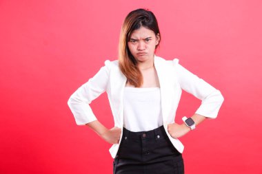 A woman in a white jacket is pouting with her hands on her hips, wearing a watch, and black pants, isolated on a red background