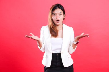 Beyaz ceket ve siyah pantolon giyen, ağzı açık, elleri açık, şaşırmış, kırmızı arka planda izole bir kadın.
