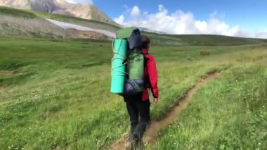 Sırt çantalı bir adam dağ yolunda yürüyor. Yazın dağlarda tatiller