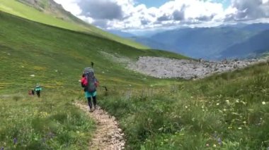 Sırt çantalı bir adam dağ yolunda yürüyor. Yazın dağlarda tatiller