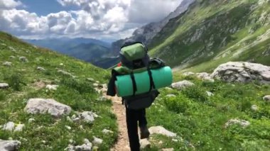 Sırt çantalı bir adam dağ yolunda yürüyor. Yazın dağlarda tatiller