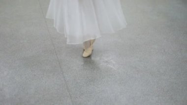 Karanlık bir sahnede ya da stüdyoda egzersiz yapan bir balerinin yakın çekimi. Sivri uçlu ayakkabılı kadın bacakları. Balerin klasik bale adımlarını gösteriyor. Yavaş çekim