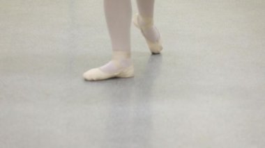 Karanlık bir sahnede ya da stüdyoda egzersiz yapan bir balerinin yakın çekimi. Sivri uçlu ayakkabılı kadın bacakları. Balerin klasik bale adımlarını gösteriyor. Yavaş çekim
