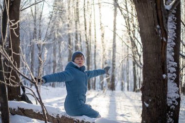 Kız ormandaki devrilmiş bir ağacın üzerinde dinleniyor. Açık hava aktiviteleri. Kışın ormanda yürü.