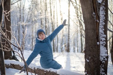 Kız ormandaki devrilmiş bir ağacın üzerinde dinleniyor. Açık hava aktiviteleri. Kışın ormanda yürü.