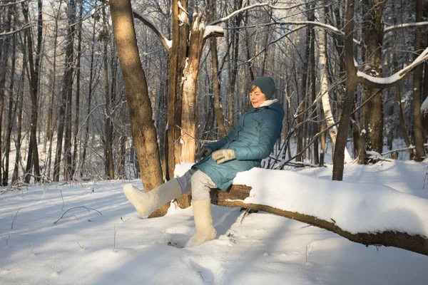 The girl is resting on a fallen tree in the forest. Outdoor activities. Walk in the forest in winter