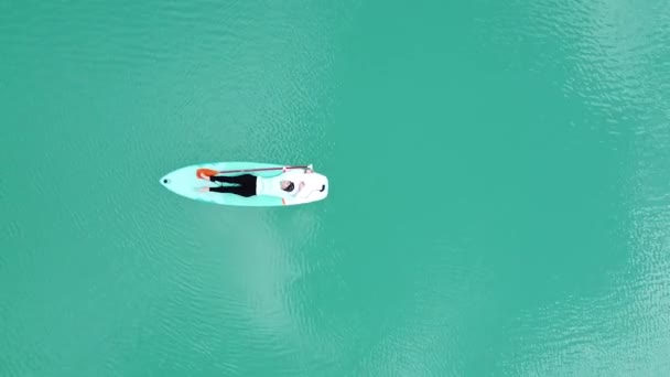 少女はターコイズブルーの水で池の上のサパで日光浴をしている カメラが高くなる 空中写真 — ストック動画