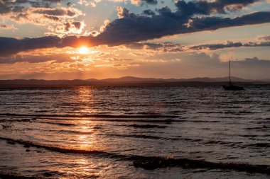 Gün batımında dağ gölü. Yat dalgalarda sallanıyor. Gün batımında bir kızın silueti