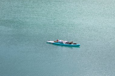 Kız turkuaz suyla bir gölde güneşleniyor.