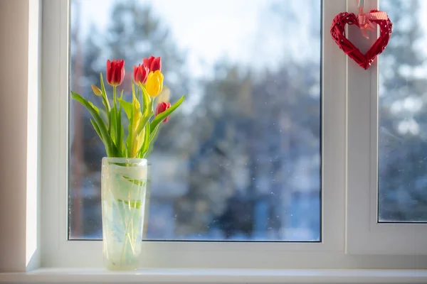 A bouquet of flowers is on the window. Outside the window, a sunny frosty snowy morning