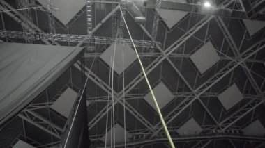 Tepedeki ışıklar tavan donanımı ızgarasında parlıyor. Yoğun gölgeler, askıya alınmış akustik panelleri açığa çıkarıyor. Yapılar modern mekanı şekillendirir