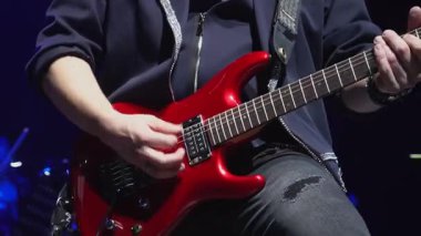 Adam yakın çekimde bas gitar çalıp seyircileri eğlendiriyor. Siyah ceketli yetenekli müzisyen sahnede telli çalgılar çalıyor.