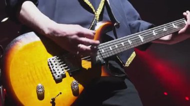 Şık ceketli gitarist gece kulübünde kırmızı ışıklara karşı müzik çalıyor. Müzisyen sahnede elektrikli müzik aleti besteliyor.