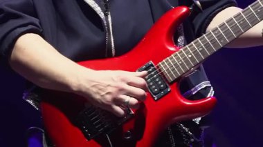 Erkek müzisyen, gece kulübünde seyircilerin önünde bas gitar çalar. Gitarist sahnede elektirikli çalgılarda solo çalıyor.