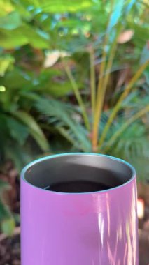 Sıcak kahveli mor termal bardak ve bulanık yeşil arka planda bir duman veya buhar izi.