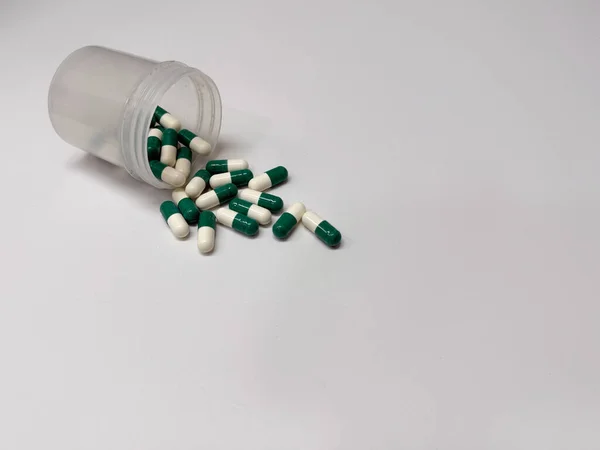  İlaç şişesindeki yeşil ve beyaz haplar beyaz arka plana döküldü - sağlık ve sağlık kavramı 