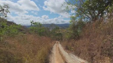 Dik, dar bir taş yolun yüksek açılı manzarası güneşli bir yamaçtan kasabaya doğru dönüyor.